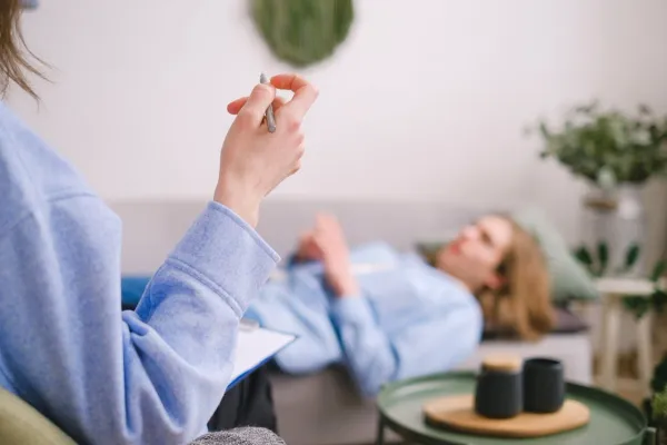 Séance de thérapie avec un psychologue prenant des notes pendant qu’un patient s’exprime sur un canapé
