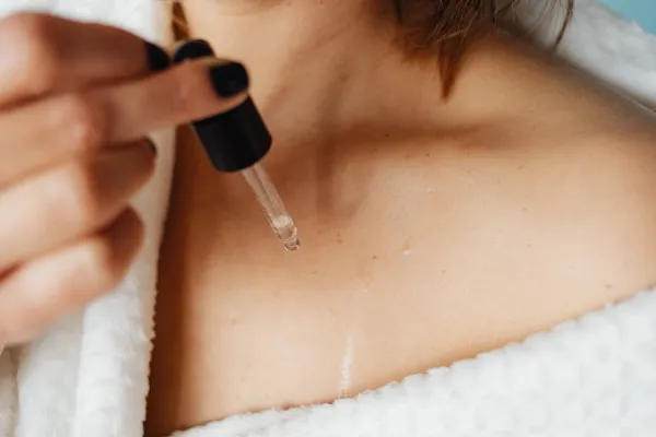 Pipette de sérum appliquant une goutte sur le décolleté féminin, soin visage et cou sur peau nue naturelle
