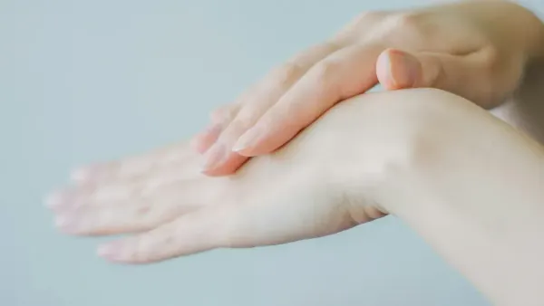 Mains féminines soignées appliquant délicatement une crème hydratante, peau claire et ongles naturels.