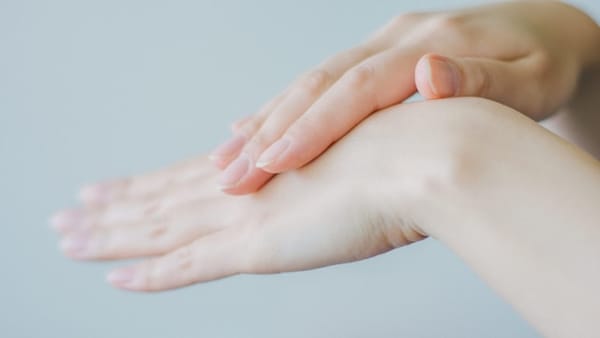 Mains féminines soignées appliquant délicatement une crème hydratante, peau claire et ongles naturels.