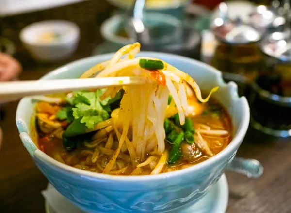 Bol de soupe de nouilles asiatiques épicée avec légumes frais, tenu avec des baguettes